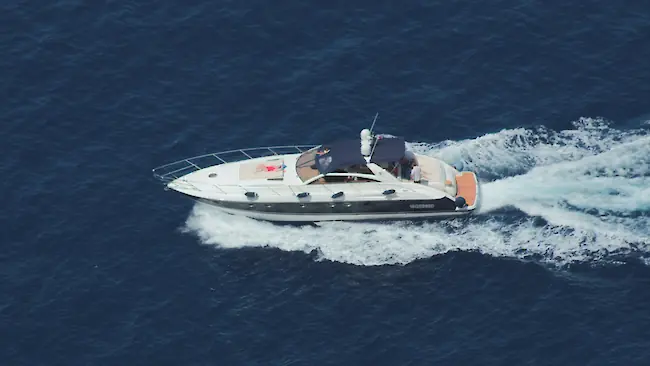 A sleek white motor yacht cutting through deep blue sea water, viewed from above as it leaves a foamy wake behind. A sleek white motor yacht cutting through deep blue sea water, viewed from above as it leaves a foamy wake behind.